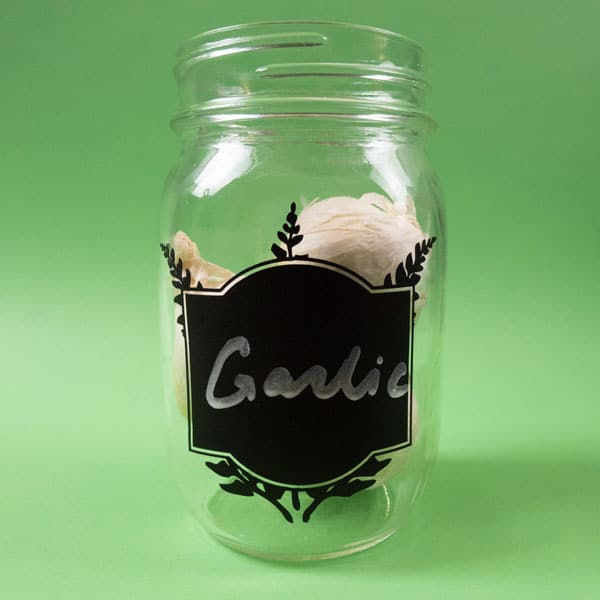 A mason jar holding garlic with a Chalkboard SpecialtyPSV on it and the world "garlic" written in chalk
