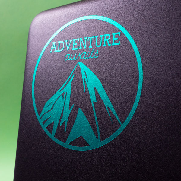 A laptop with a Polished Metal SpecialtyPSV™ sticker that reads "Adventure Awaits"