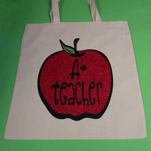 A tote bag with our A+ Teacher cut file made with Black ThermoFlex® Plus Matte and Red & Light Green GlitterFlex® Ultra