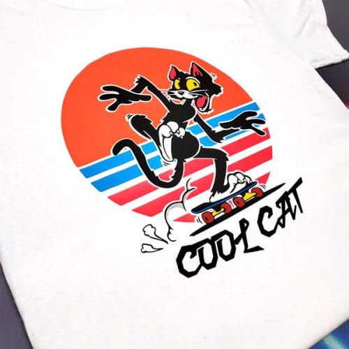 A shirt that says "Cool Cat" with a cat on a skateboard with a sunset in the background